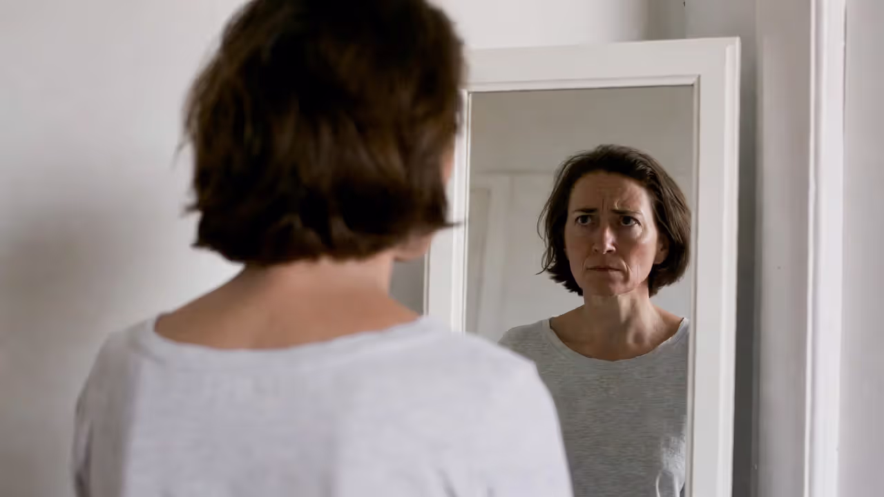 Person looking into a mirror where the reflection appears calmer and more confident than the real expression.